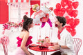 Two people at a Valentine's Day table with Cupid foil balloon and red heart balloons in romantic setting